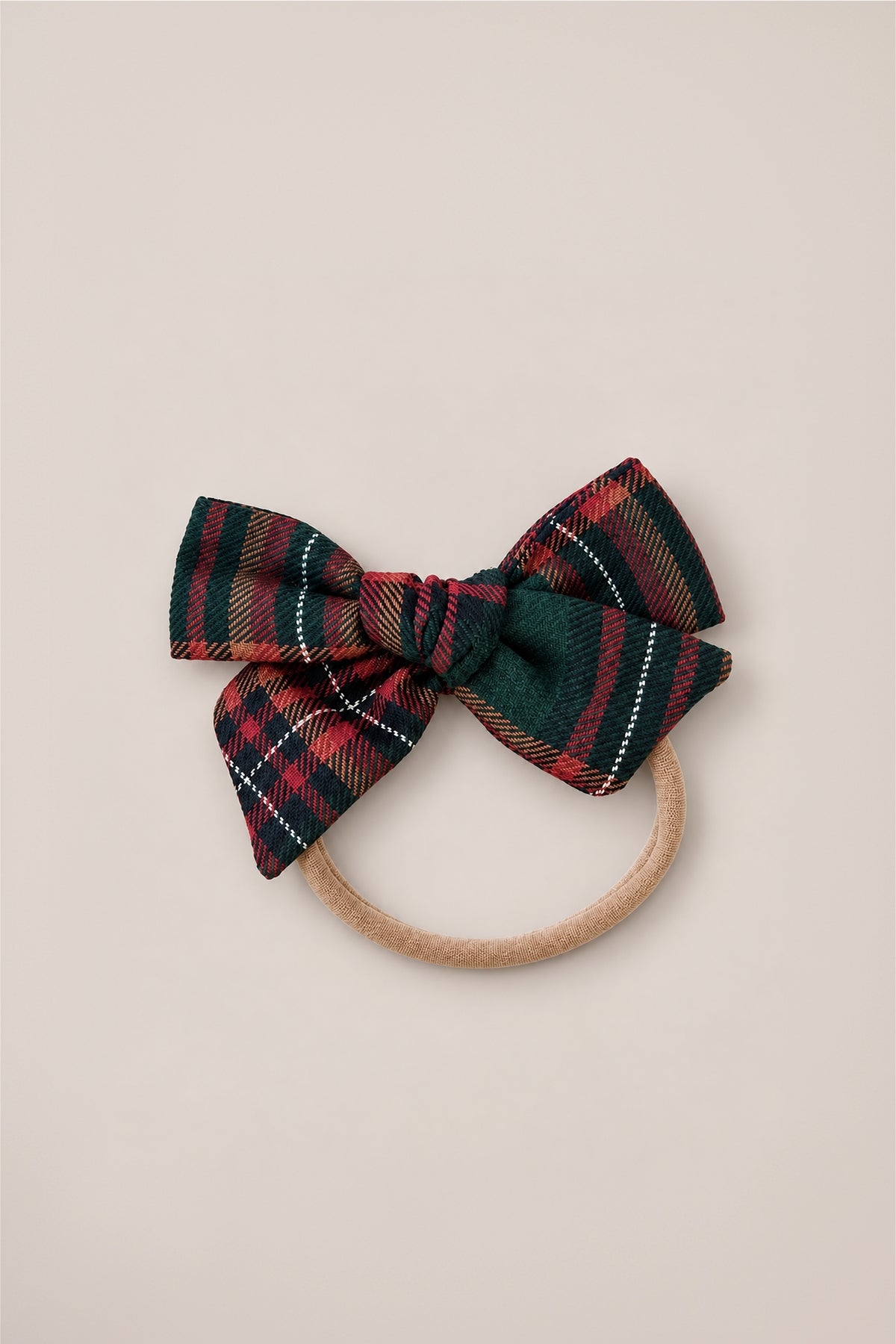 The Hair Bows in Evergreen Plaid by Ivy City Co feature a charming dark green, red, and gold cotton flannel bow attached to a beige elastic hair tie, shown on a simple light background—perfect as a festive holiday headband accessory.