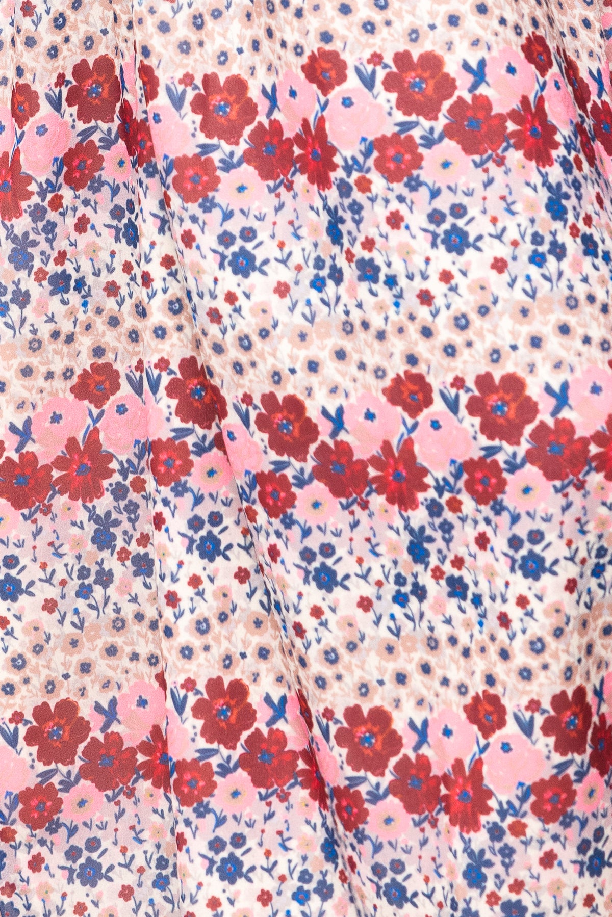Close-up of the Hayden Dress in Lush Garden by Ivy City Co, showing pleated white fabric with red, pink, and blue flowers arranged in horizontal rows alongside small leaves and dots.