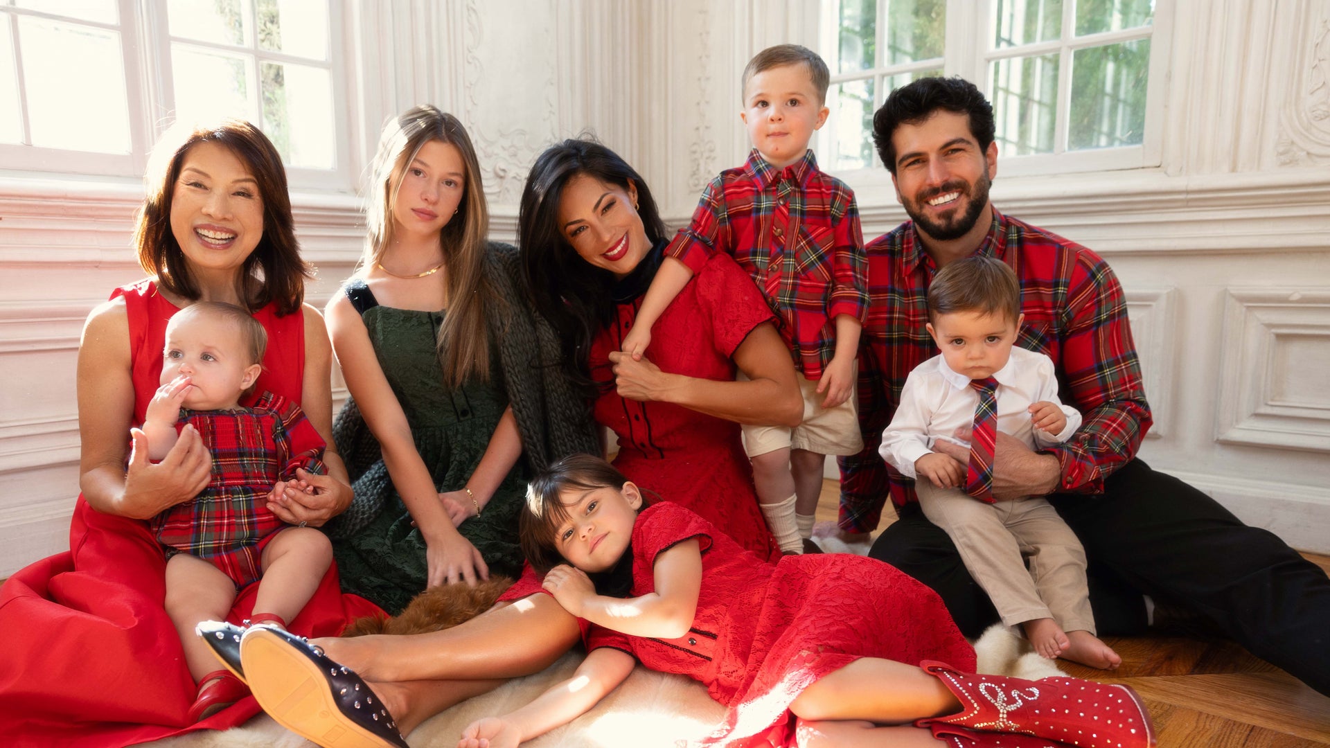 Family of seven posing together in a well-lit room with white walls and large windows.