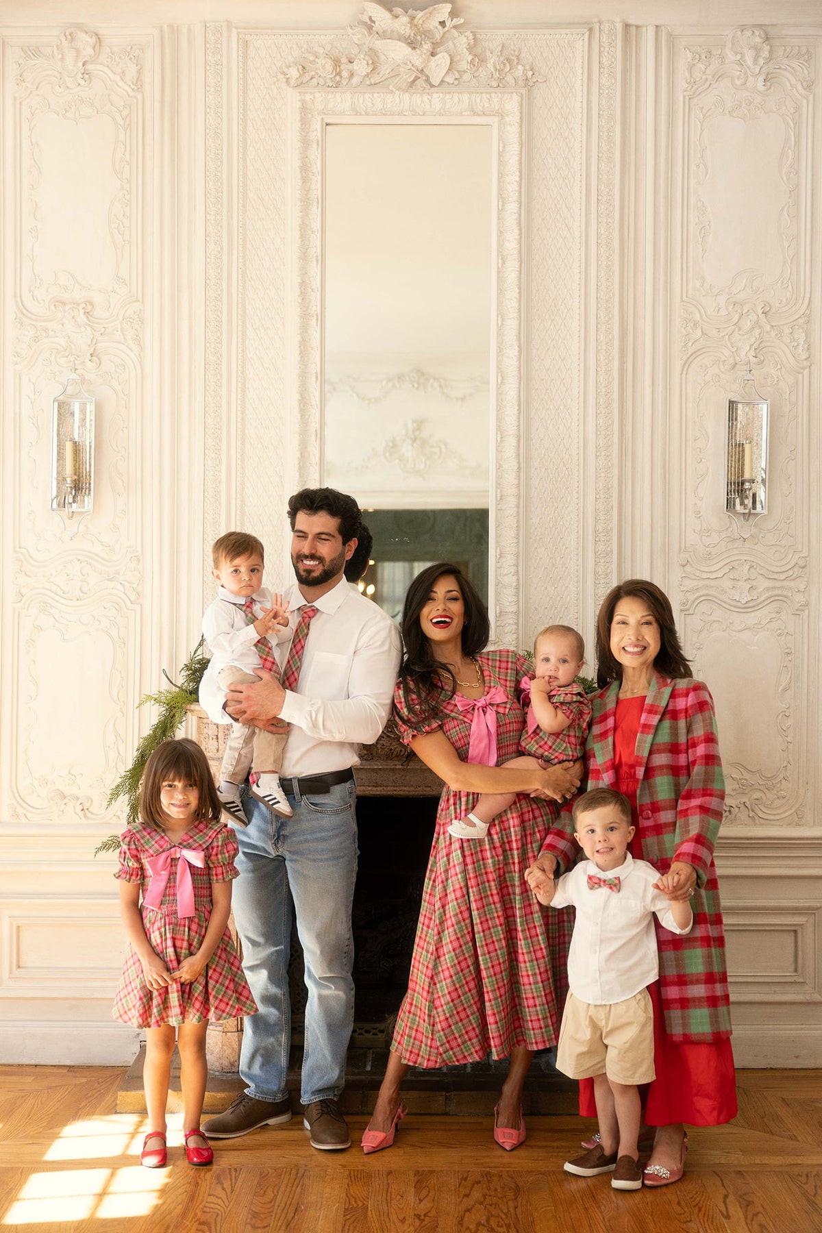 A family of seven children and adults stand in front of a fireplace