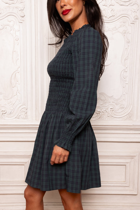 Woman wearing a plaid dress against a decorative white wall.