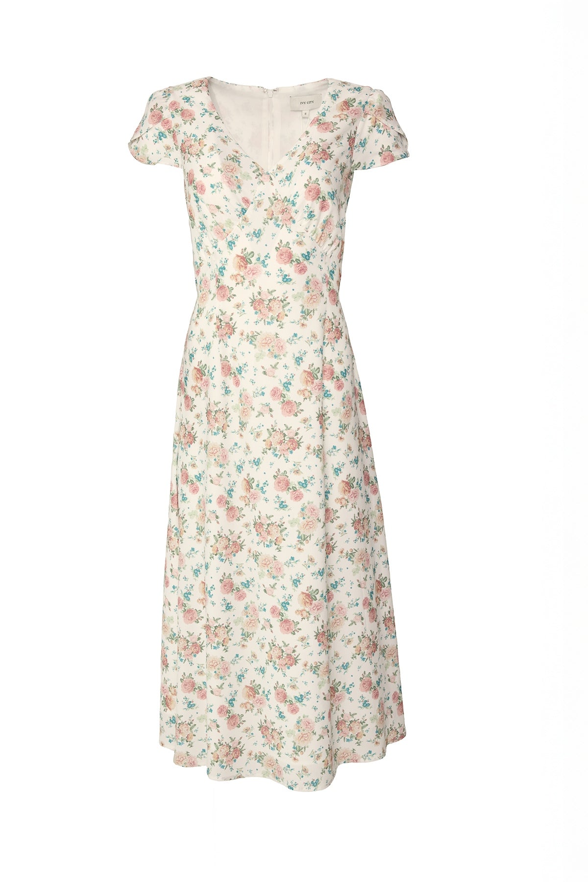 The Ivy City Co Fiona Dress in Countryside Peony Blossom features a light, short-sleeve V-neck design with a fitted waist and delicate pink, blue, and green floral prints on white. Shown against a plain white background.