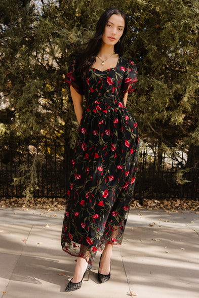 Woman wearing a black floral dress standing outdoors with trees in the background