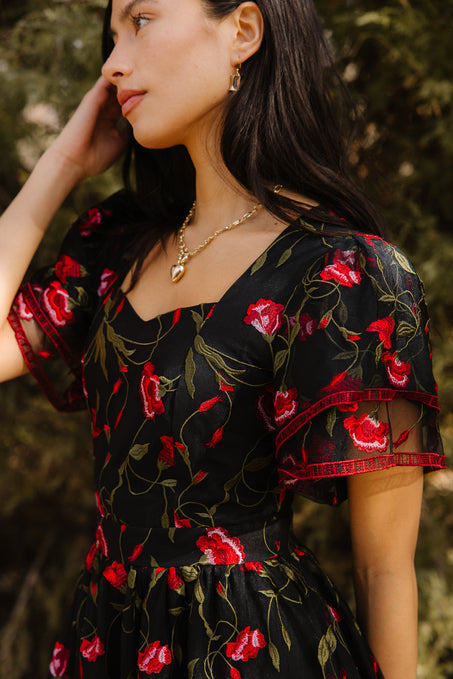 Woman wearing a black floral dress standing outdoors with trees in the background