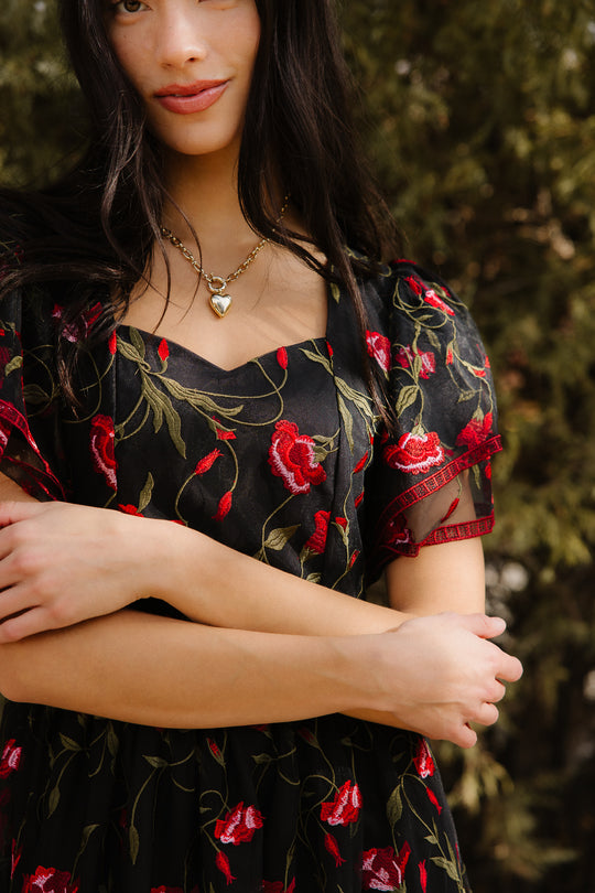 Woman wearing a black floral dress standing outdoors with trees in the background