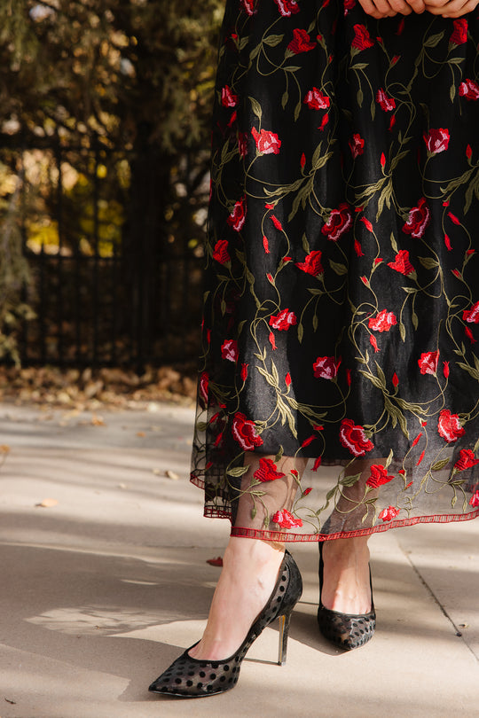 Bottom half of a black floral dress outside in front of trees 