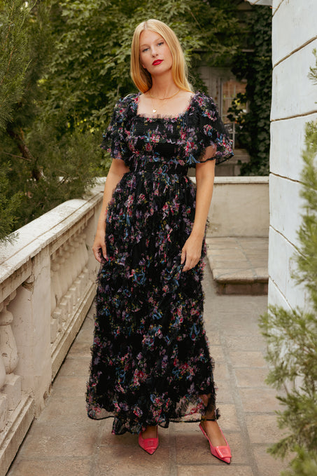 Woman wearing a black floral dress with a blurred outdoor background