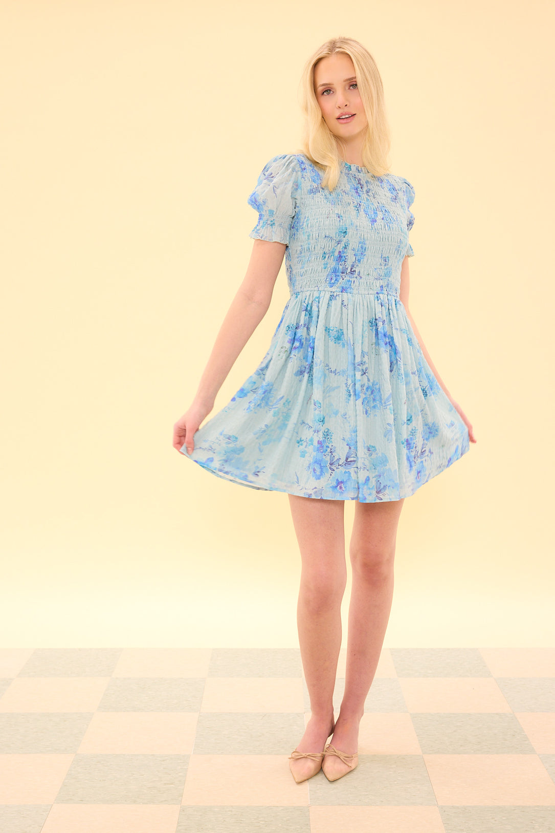 Woman wearing a light blue floral dress on a checkered floor with a beige wall background