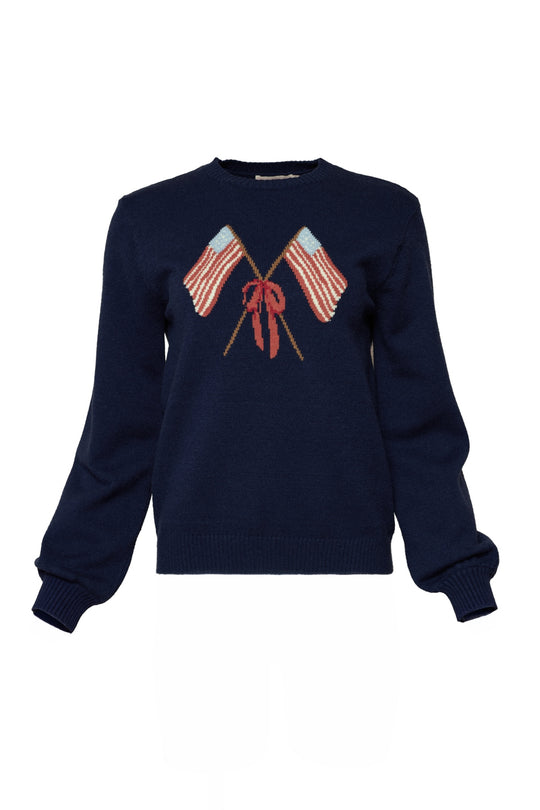 The Ivy City Co Freedom Sweater in Midnight is a navy, lightweight crewneck with long sleeves, featuring two crossed American flags with red, white, and blue stripes and a red bow on the chest for a patriotic touch.