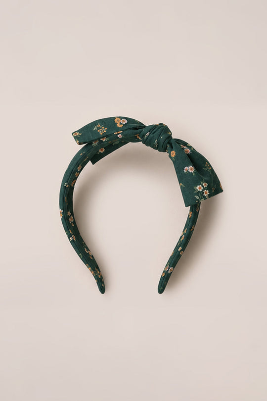 The Ivy City Co Hair Bows in Evergreen Lovelorn Ditsy feature a dark green headband made from soft cotton, adorned with a delightful floral print and topped with a charming bow, beautifully displayed against a simple light background.