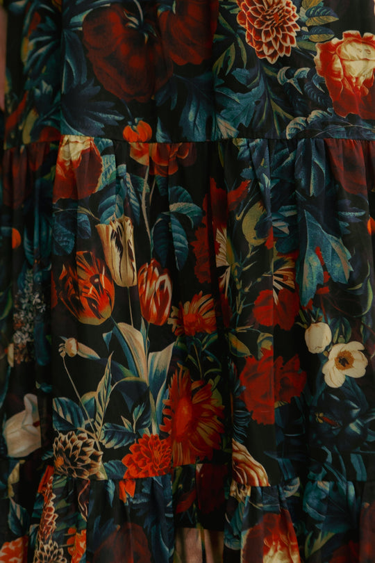 Close-up of the Cordelia Dress in Moody Floral by Ivy City Co, featuring a vibrant floral pattern in red, orange, cream, and green hues on a black background. The fabric is slightly gathered or tiered, making this chiffon midi dress ideal for maternity-friendly fall wear.