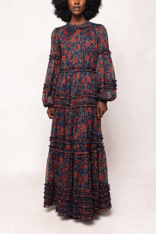 Woman wearing a long, dark blue floral dress with red patterns on a white background
