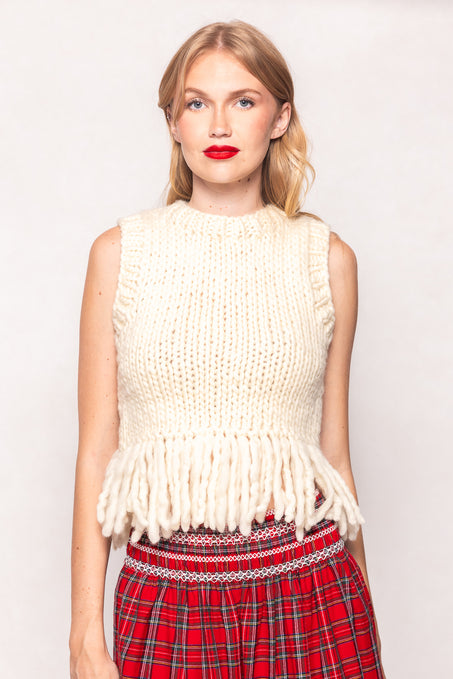 Woman wearing a white knitted vest with fringe and a red plaid skirt on a plain background