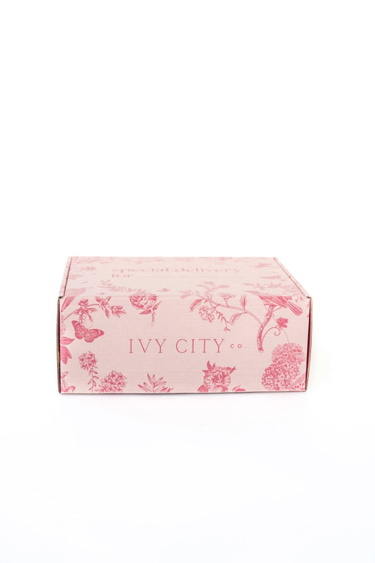 A light pink Gift Box from Ivy City Co, featuring red floral designs and the brand’s name printed on the front, shown against a plain white background.