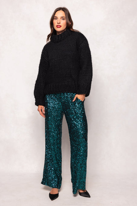 Woman wearing a black sweater and teal sequin pants on a white background