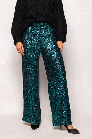 Person wearing teal sequin pants and a black sweater on a white background