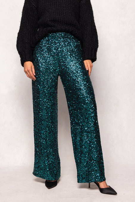 Person wearing teal sequin pants and a black sweater on a white background