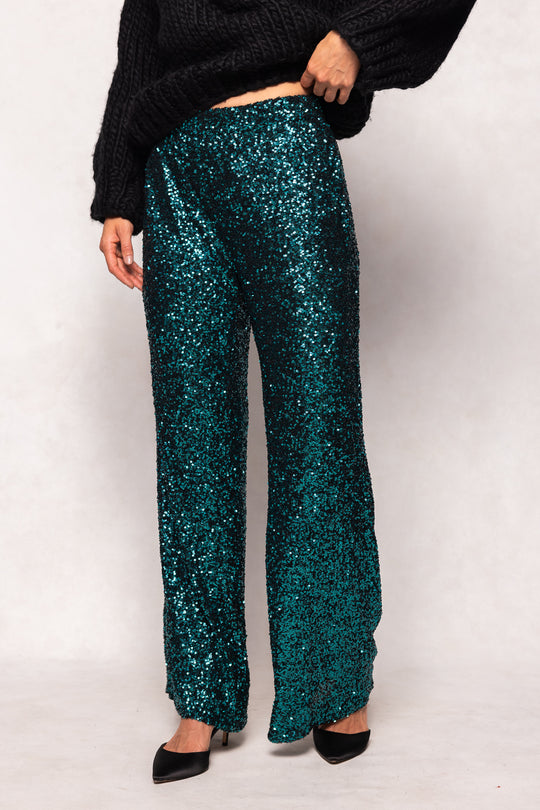 Teal sequin pants worn by a person on a white background