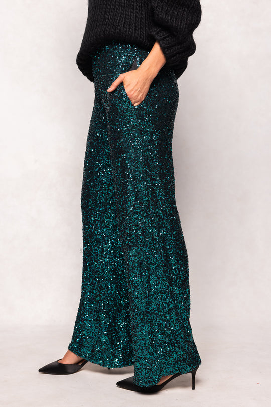 Person wearing a teal sequin skirt with a plain background