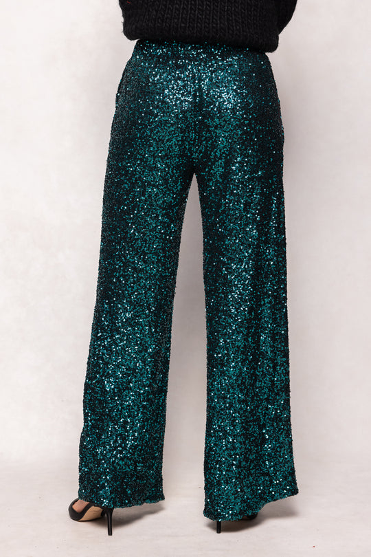 Teal sequin pants worn by a person on a white background