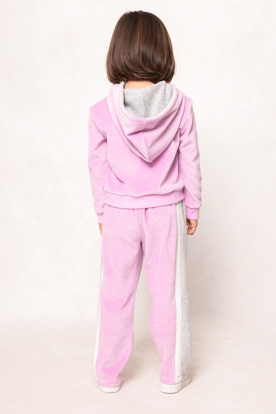 A young child with brown hair stands facing away, wearing the Ivy City Co Mini Kailey Zip Up Velour Sweatshirt in Pink and white shoes, against a plain light background.