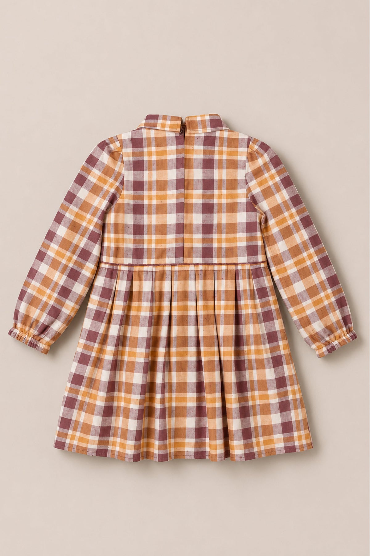 The Mini Bowie Long Sleeve Dress in Spiced Plaid by Ivy City Co is a children’s long-sleeve cotton dress featuring a fitted bodice, gathered skirt, and elasticized cuffs. Showcased from the back on a neutral background, it displays a plaid pattern in shades of brown, yellow, and white.