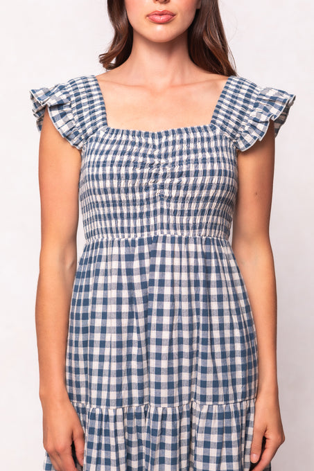 A woman models the Ivy City Co Hailey Dress in Indigo Gingham, featuring ruffled cap sleeves and a smocked bodice, shown from shoulders to mid-thigh against a plain light background.
