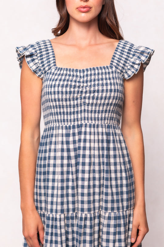 A woman models the Ivy City Co Hailey Dress in Indigo Gingham, featuring ruffled cap sleeves and a smocked bodice, shown from shoulders to mid-thigh against a plain light background.