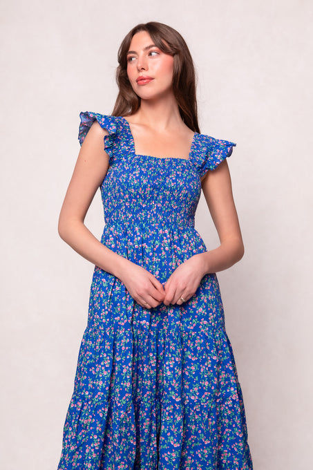 Woman wearing the Ivy City Co Hailey Dress in Allie Blue Floral, a maternity-friendly style with ruffled shoulder straps, standing against a plain light background and gazing slightly to the side.