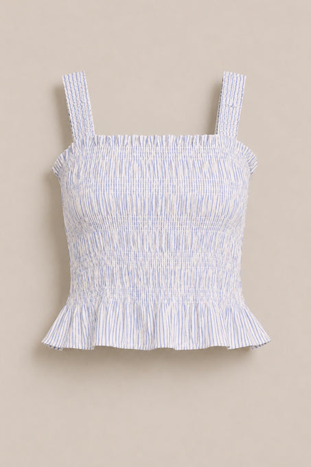 The Ivy City Co Harley Top in Blue & White Pinstripe features smocking, wide shoulder straps, and a ruffled hem. This sleeveless top is shown against a plain beige background.