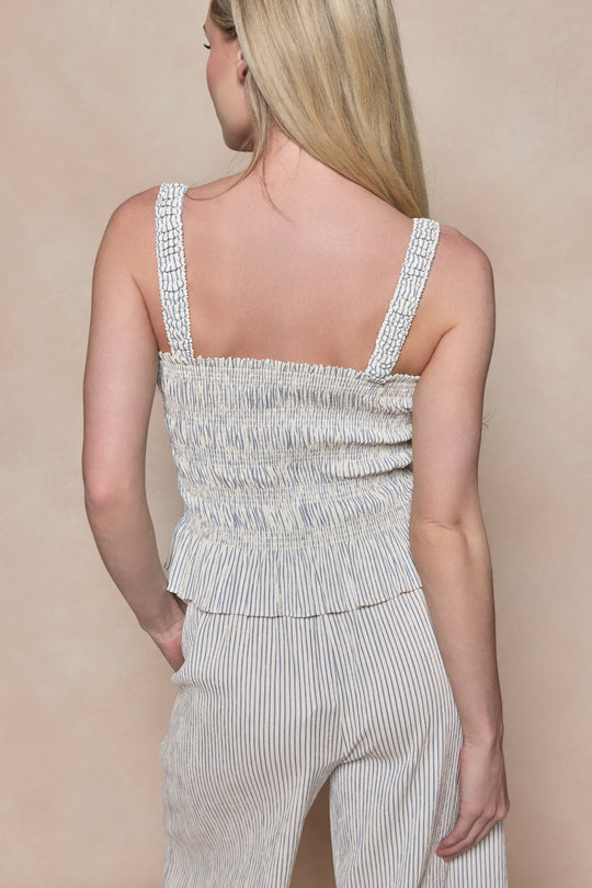 A woman with long blonde hair is shown from the back wearing the Ivy City Co Harley Top in Blue & White Pinstripe, paired with matching high-waisted pinstriped pants, against a beige background.