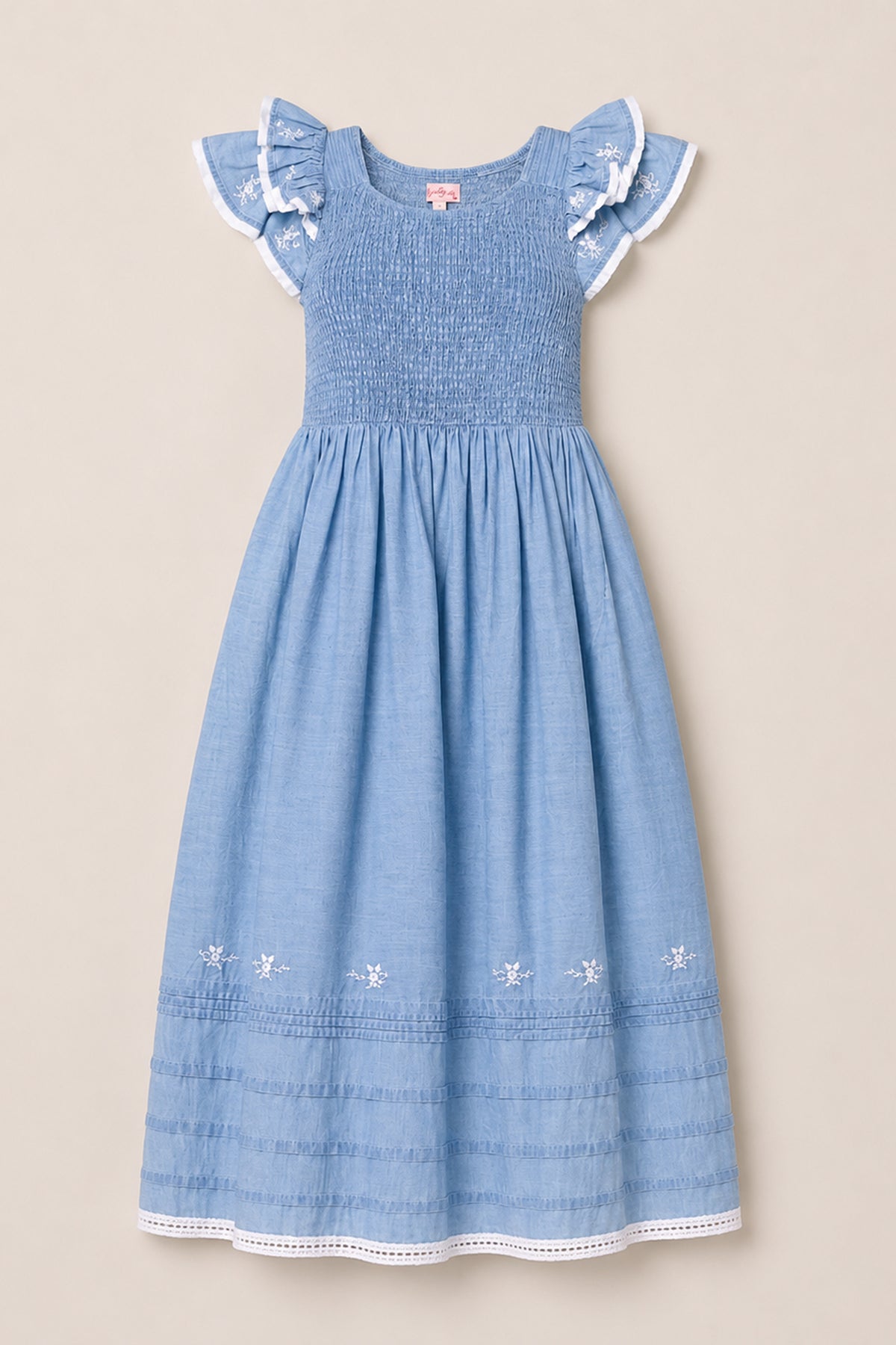 The Ivy City Co Hattie Ankle Length Dress in Embroidered Chambray is a light blue, sleeveless dress for girls, featuring ruffled lace-trim sleeves, a smocked bodice for comfort and style, and delicate embroidered flowers along the hem. Displayed on a neutral background, this charming dress is maternity friendly, making it a versatile addition to any wardrobe.
