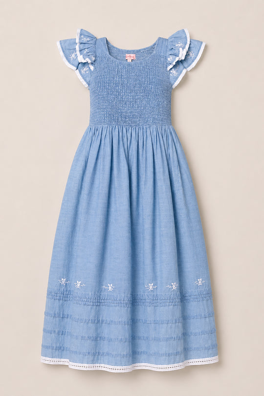 The Ivy City Co Hattie Ankle Length Dress in Embroidered Chambray is a light blue, sleeveless dress for girls, featuring ruffled lace-trim sleeves, a smocked bodice for comfort and style, and delicate embroidered flowers along the hem. Displayed on a neutral background, this charming dress is maternity friendly, making it a versatile addition to any wardrobe.