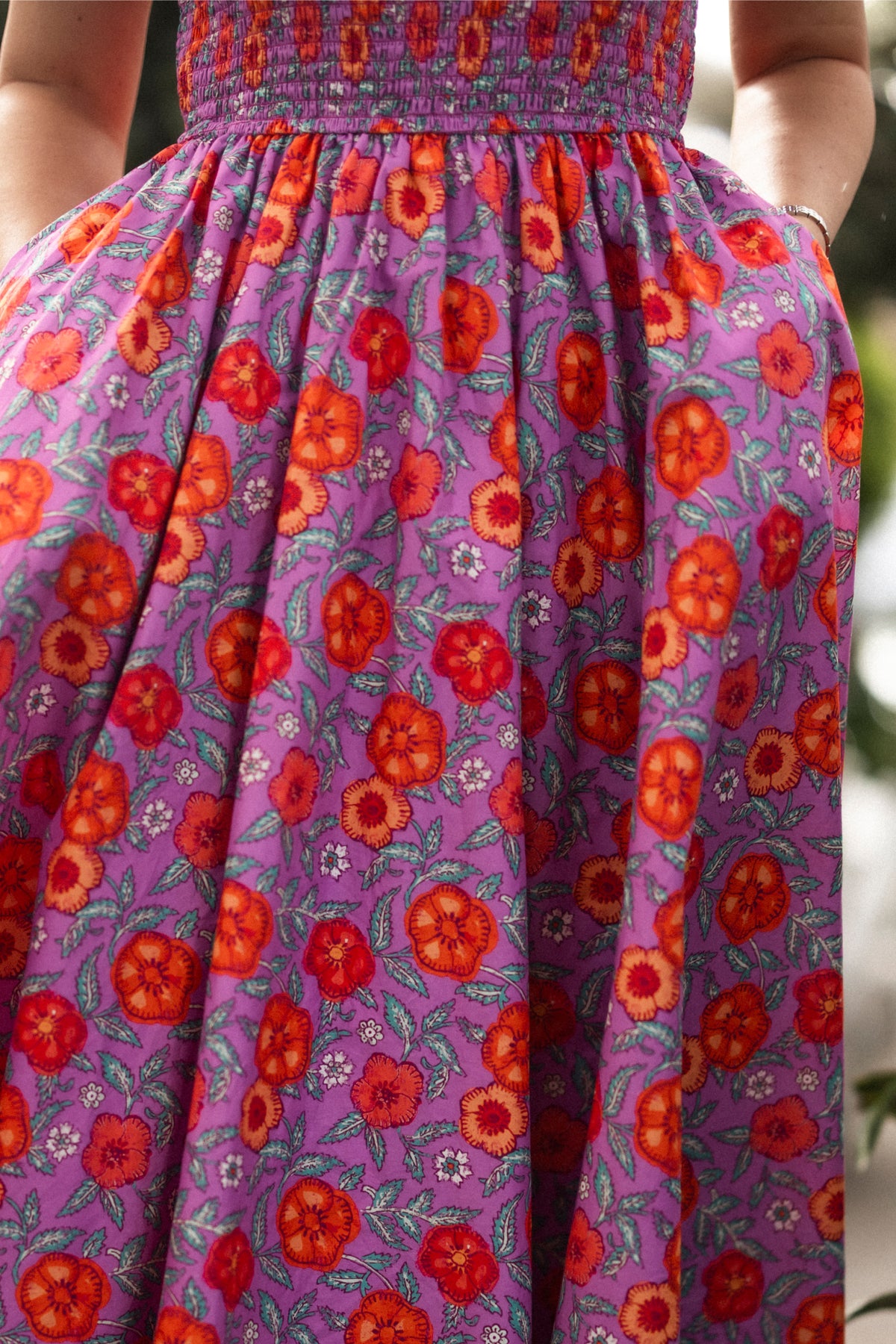A person stands outdoors in the Ivy City Co Hattie Dress in Thistle Flower Poppy Woodblock, with hands in pockets. Only the dress and part of their arms are visible. This style is nursing-friendly and comfortable for maternity wear.