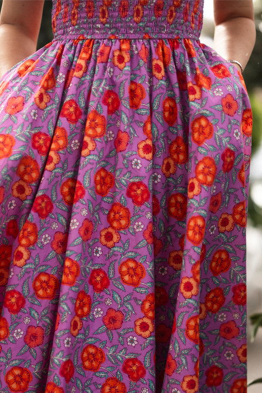 A person stands outdoors in the Ivy City Co Hattie Dress in Thistle Flower Poppy Woodblock, with hands in pockets. Only the dress and part of their arms are visible. This style is nursing-friendly and comfortable for maternity wear.