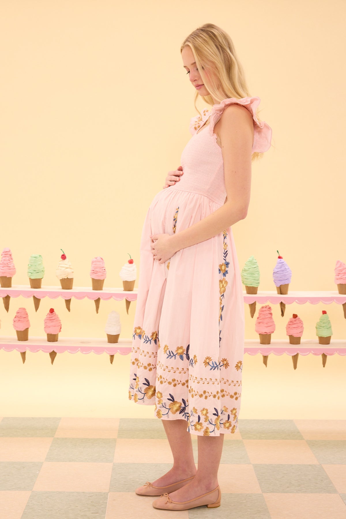 Pregnant woman in a pink dress standing in front of an ice cream stand with colorful ice cream cones.