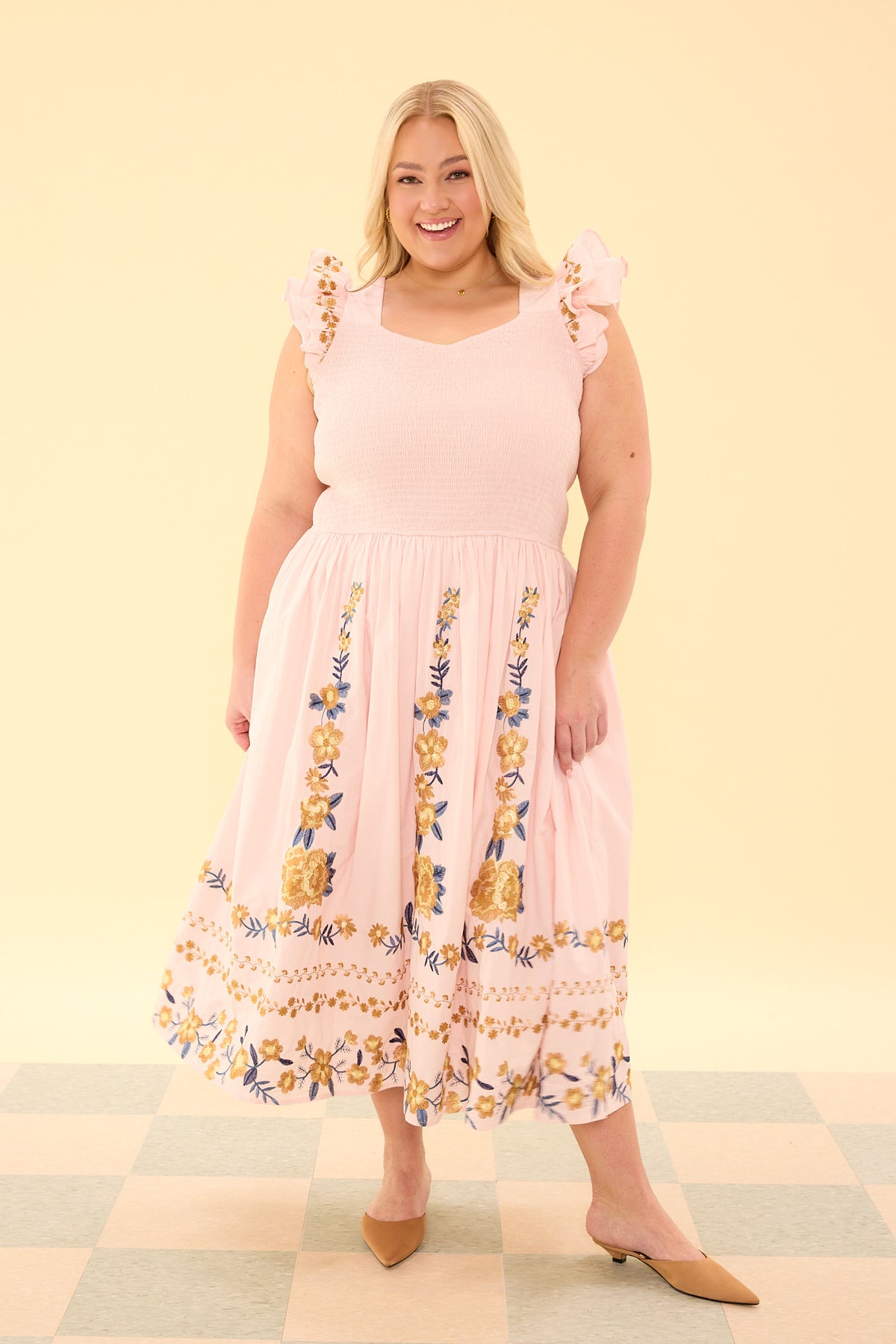 Woman wearing a pink dress with floral patterns on a checkered floor and light yellow background