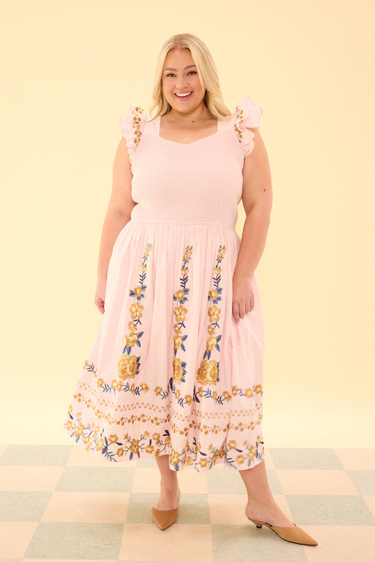 Woman wearing a pink dress with floral patterns on a checkered floor and light yellow background