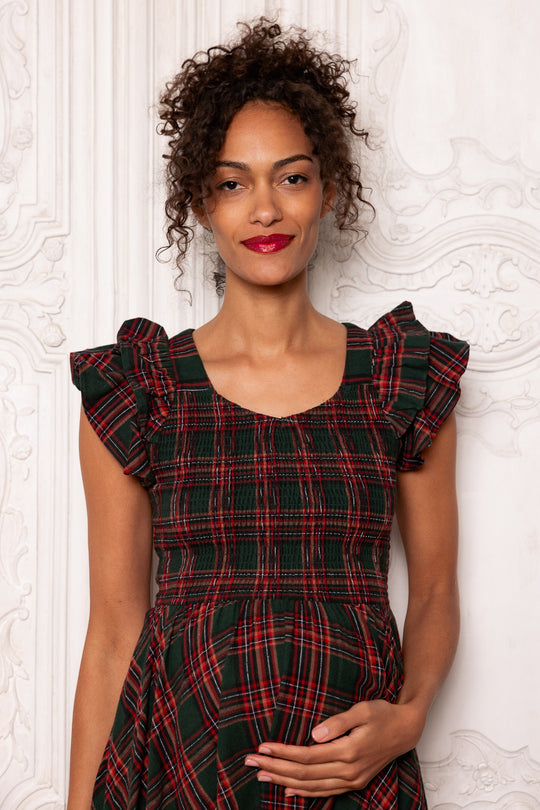 Woman wearing a red and black plaid dress against a white textured wall.