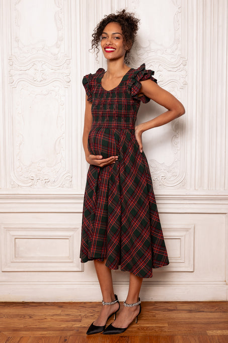 Woman wearing a red plaid dress standing against a white wall.