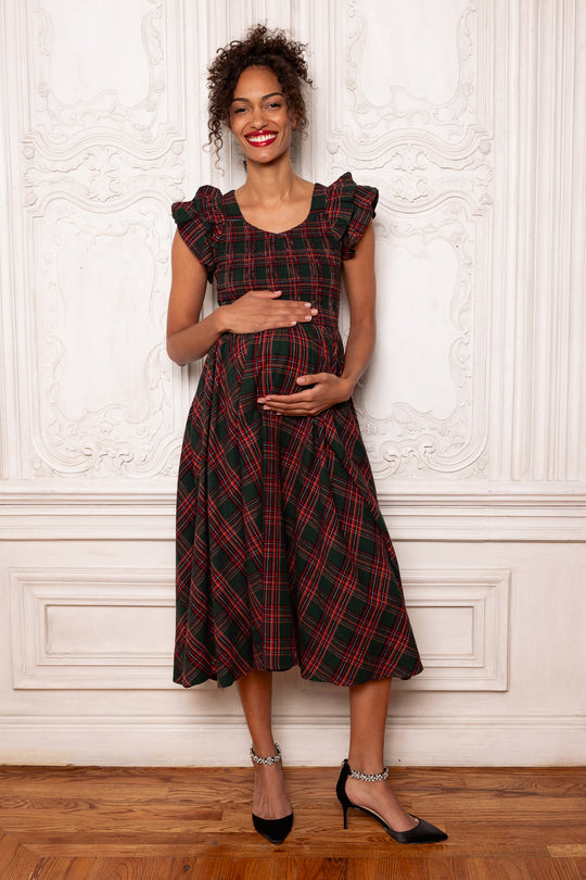 Woman wearing a red and black plaid dress standing against a white wall.