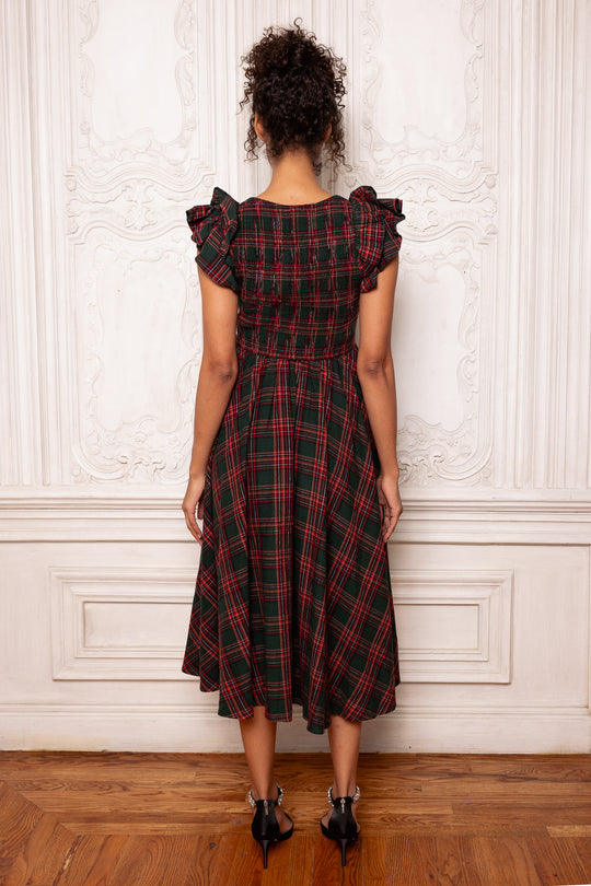 Woman wearing a red and black plaid dress against a white wall.