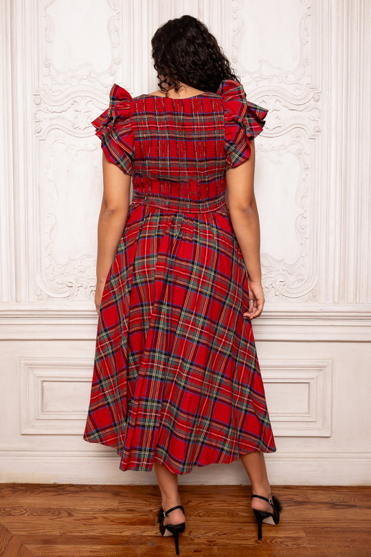 Woman wearing a red plaid dress with ruffled shoulders against a white wall.
