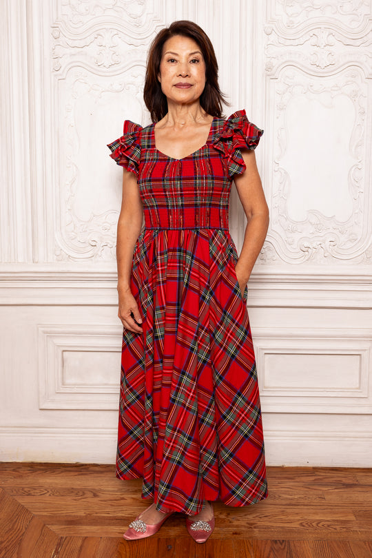 Woman wearing a red plaid dress standing against a white wall.