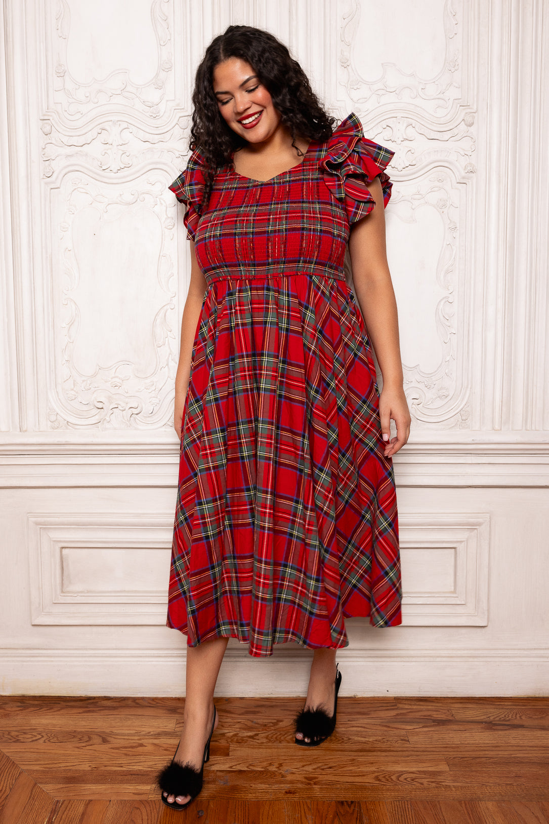 Woman wearing a red plaid dress with ruffled sleeves against a white wall.