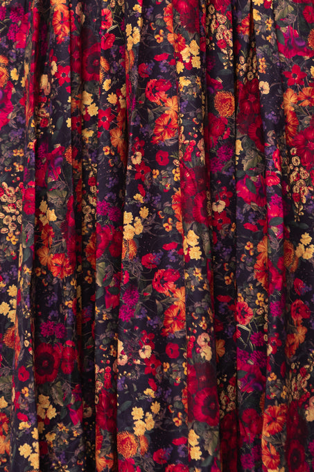 The Hattie Dress in Night Garden by Ivy City Co features a vibrant dark floral pattern with red, orange, yellow, and purple flowers—perfect as a maternity-friendly midi dress with a smocked bodice.