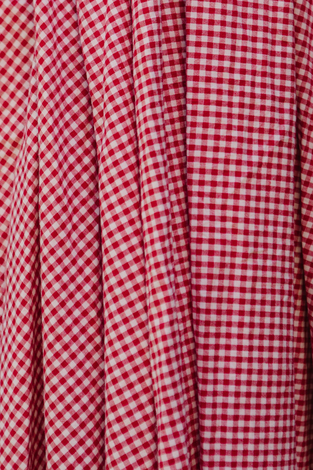 Close-up of the Hattie Dress in Red Gingham by Ivy City Co, featuring white checks, vertical pleats, and a smocked bodice for a textured look and maternity-friendly charm.