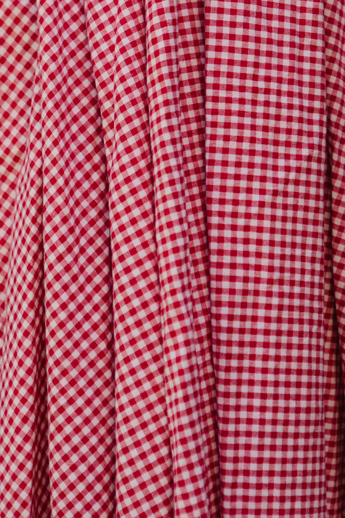 Close-up of the Hattie Dress in Red Gingham by Ivy City Co, featuring white checks, vertical pleats, and a smocked bodice for a textured look and maternity-friendly charm.