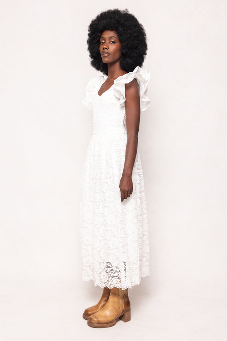 A woman with an afro stands in profile against a plain light background, wearing the Ivy City Co Hattie Dress in White Lace and tan ankle boots.