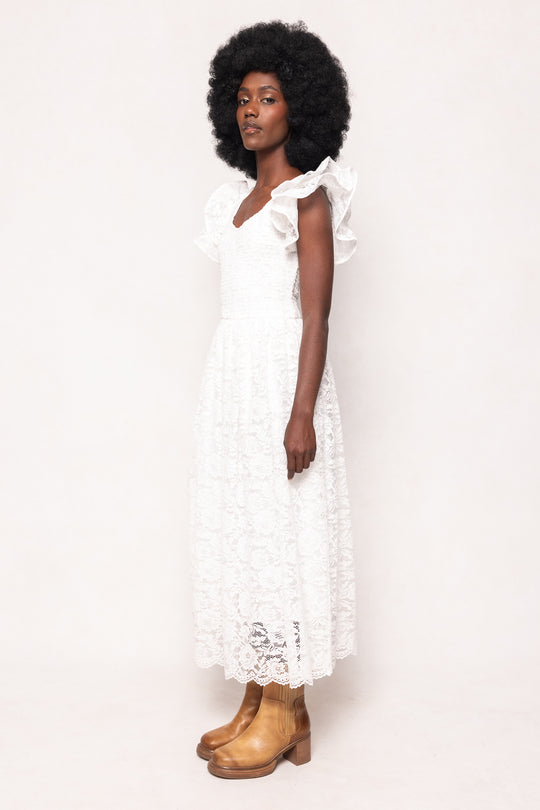 A woman with an afro stands in profile against a plain light background, wearing the Ivy City Co Hattie Dress in White Lace and tan ankle boots.